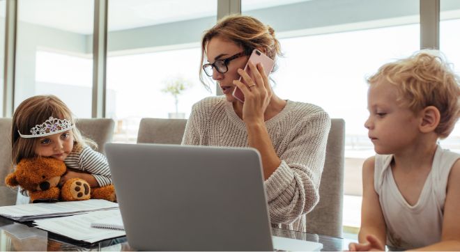 Woman sitting at dining table with her two children talks on the phone while paying a bill online