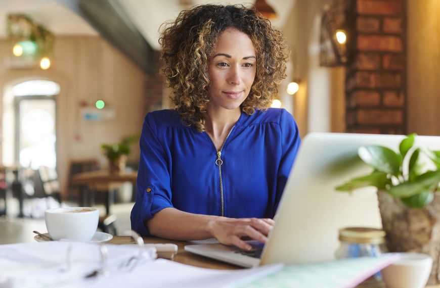 A woman sitting at a coffeeshop uses her laptop to review a digital invoice