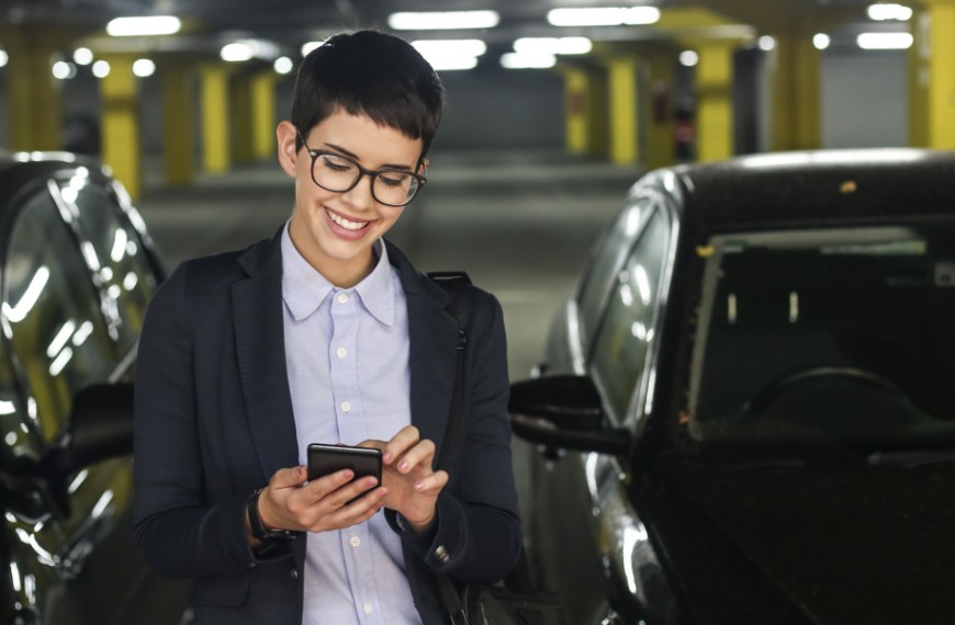 Woman in a parking garage smiles as she makes a mobile payment for her parking spot